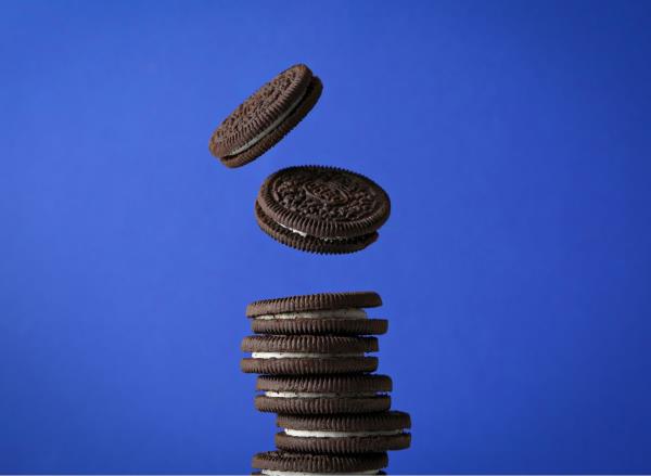 Oreo coo<em></em>kies falling on a pile in front of blue background