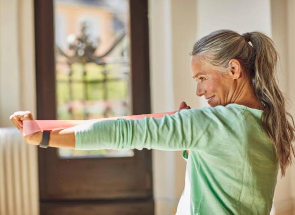 mature woman doing resistance band arm exercise at home, co<em></em>ncept of weight-bearing exercises for adults over 50