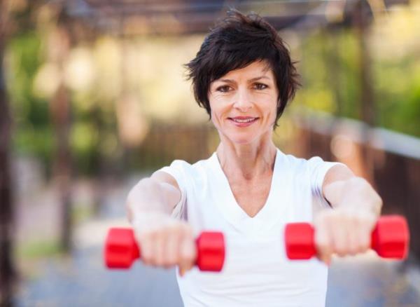 close-up of mature blo<em></em>nde woman walking while lifting dumbbells at sunset