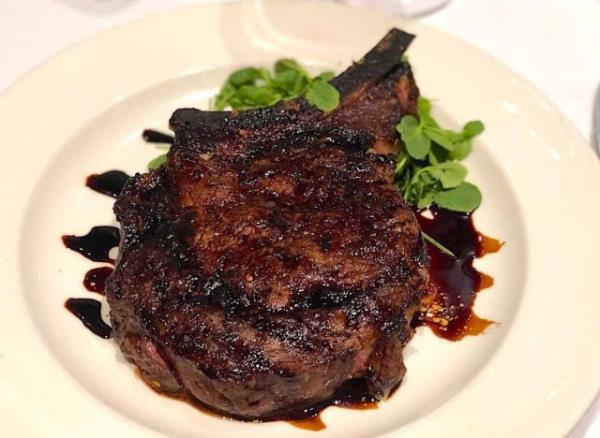 A dry-aged steak with cream sauce on a white plate, set against a vibrant background.