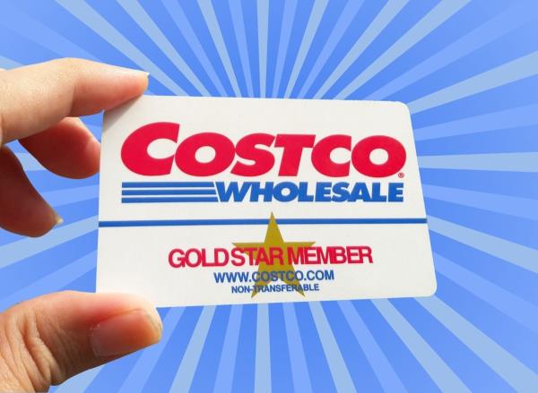 hand holding Costco membership card in front of striped blue background