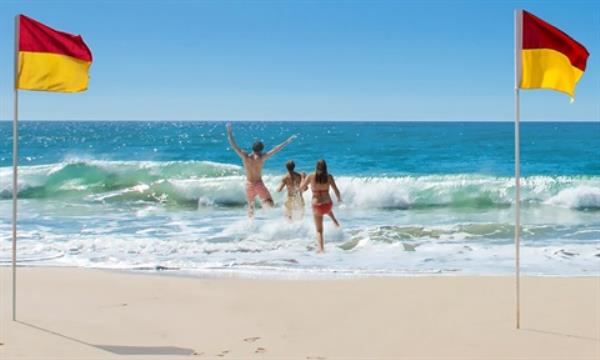 Beach goers running into the ocean between the beach safety flags