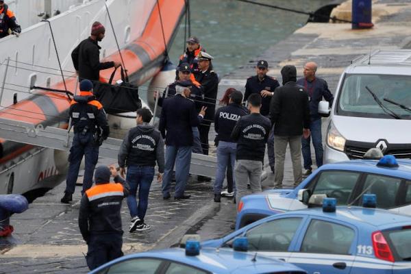 A group of Italian police meeting migrants coming off of a boat at a dock