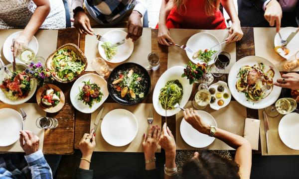 shot from above of people sat around table, hands helping themselves to food, white plates and cutlery