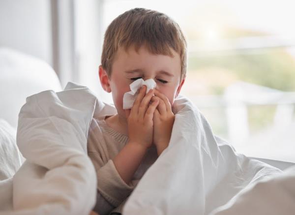 A young boy blows his nose into a tissue.