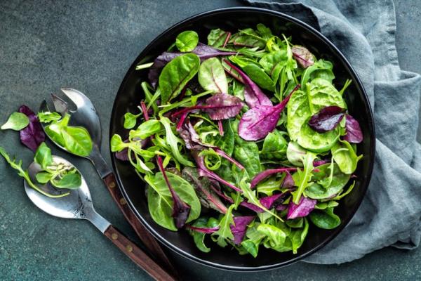 Leafy green salad in bowl on table with serving spoon