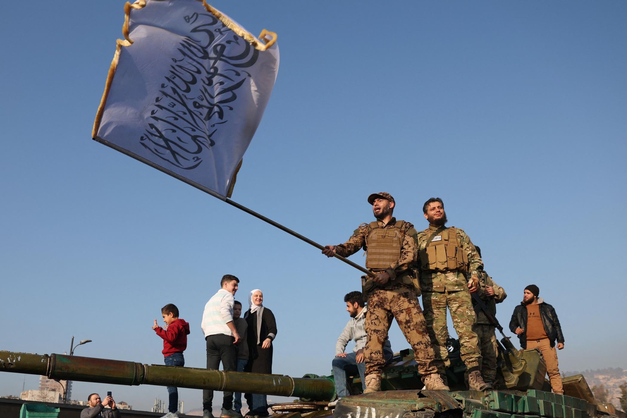 An anti-regime fighter waves a flag of his group atop a tank in Damascus, Syria, Dec. 9, 2024. (AFP Photo)